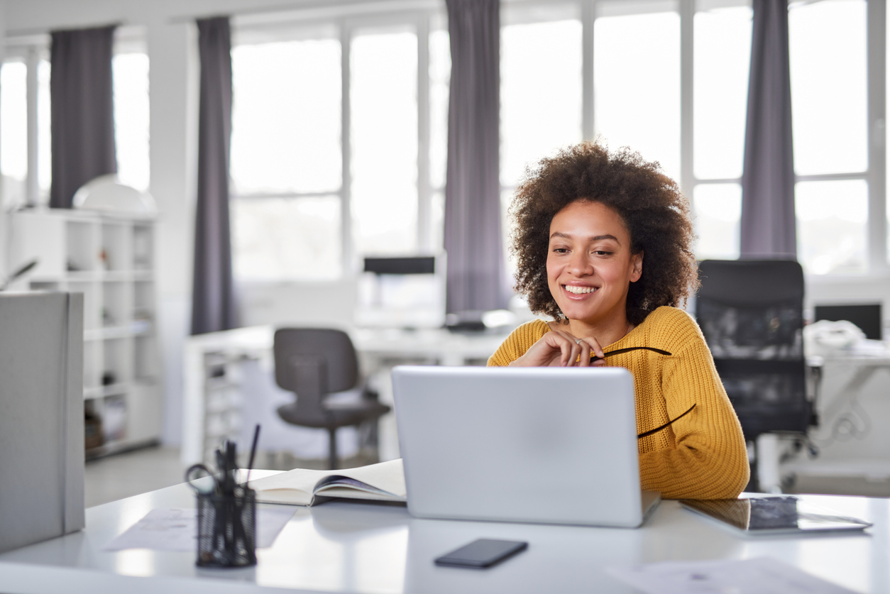 Beautiful smiling mixed race businesswoman dressed casual sitting in office and using laptop.