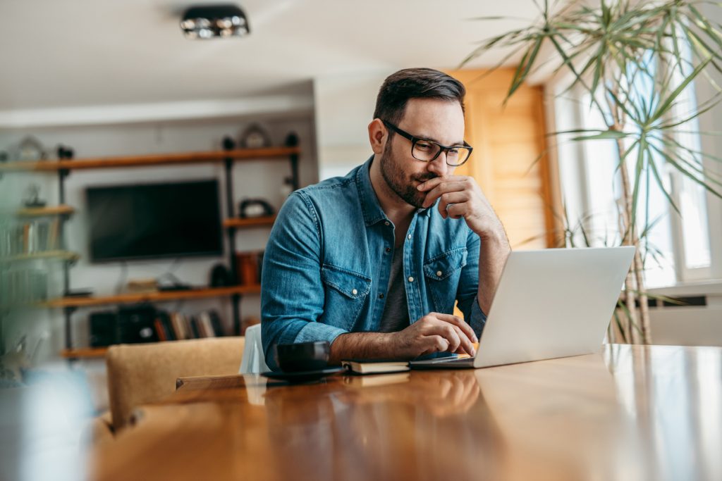 Pensive man looking at laptop while sitting at wooden table, portrait.