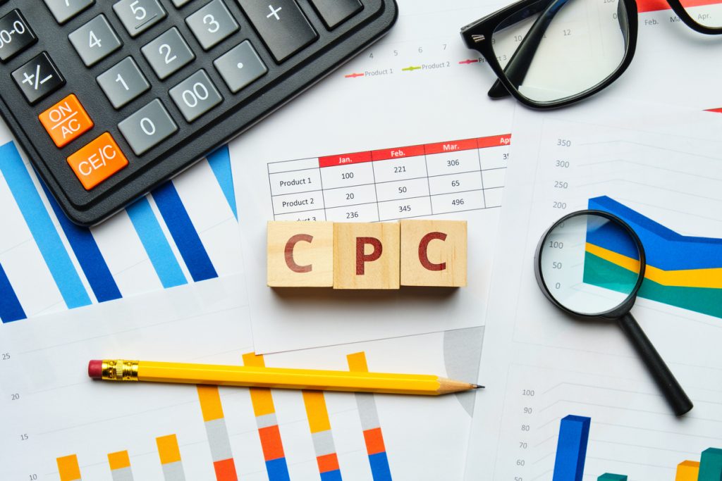 Table with CPc (or cost per click) wooden letters in the middle, surrounded by graphs, calculator and other stationary