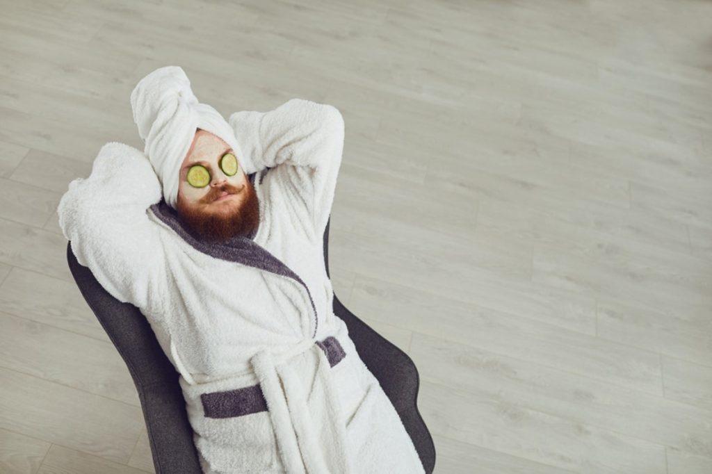 man in grey dressing gown relaxing with cucumber on their eyes