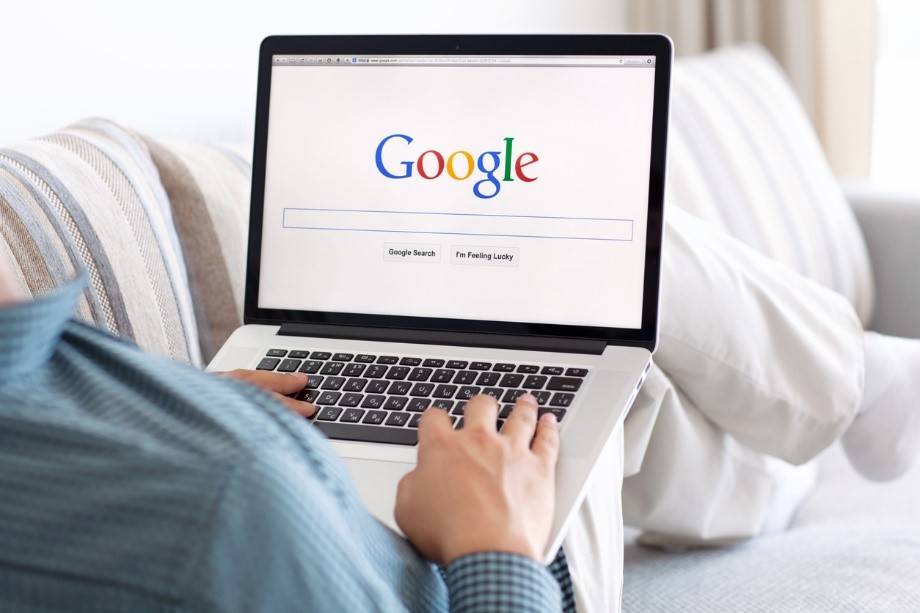 person browsing google via a laptop while sat laid back on the sofa