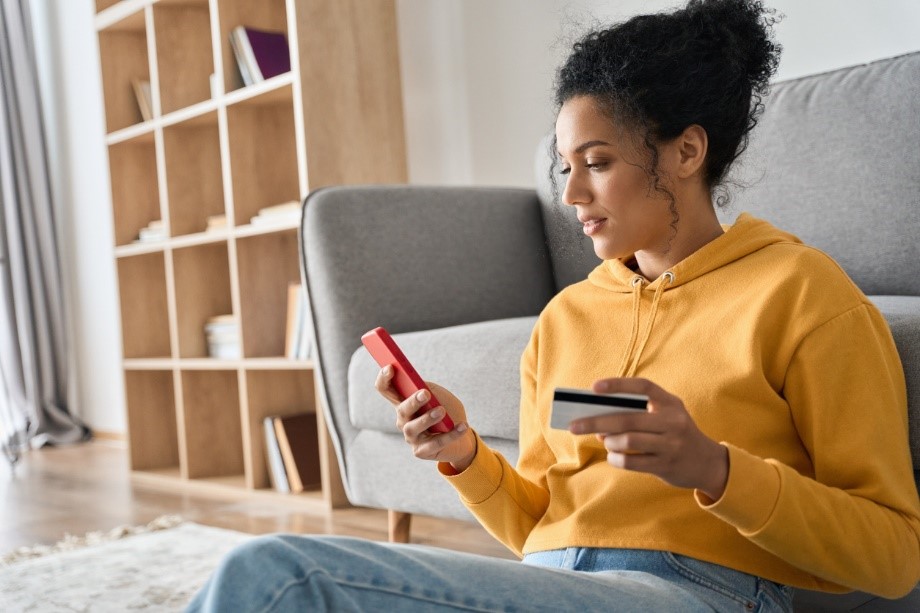 lady sat on floor with phone in one hand and bank card in the other