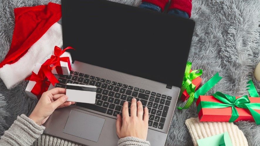 personal on laptop with bank card in one hand surrounded by presents