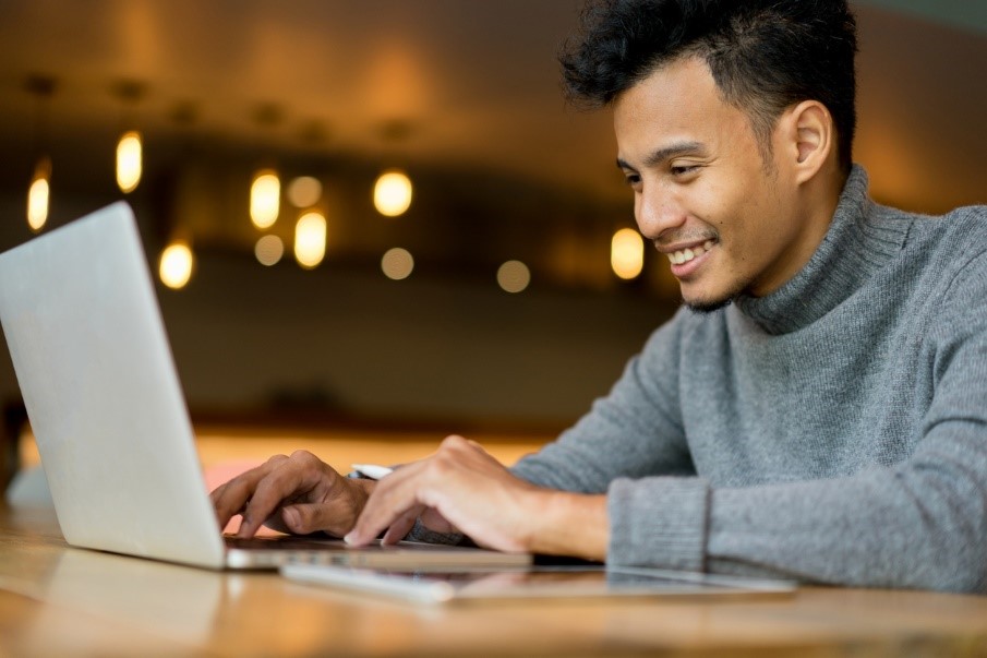 Man smiling and typing on a laptop