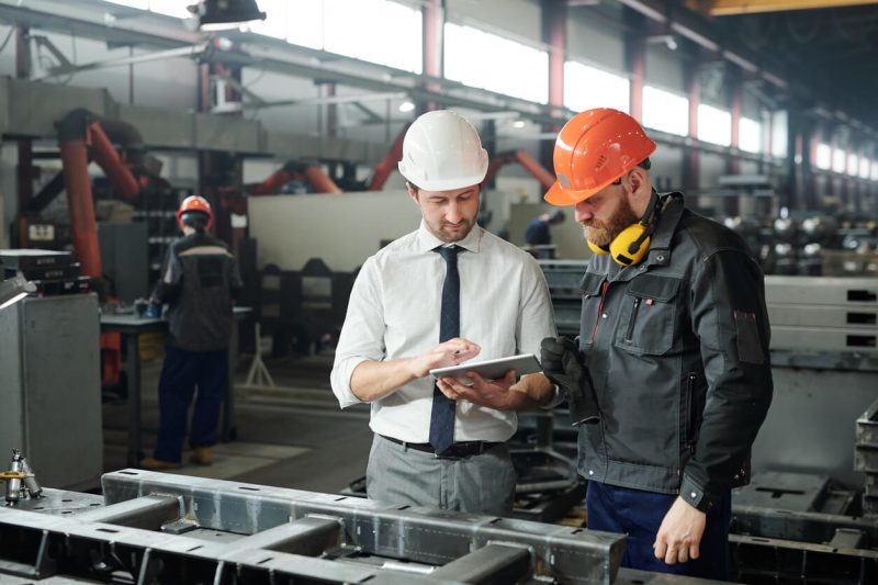 engineers discussing technical sketch on display of tablet in factory workshop