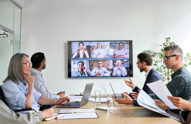 Diverse employees on online conference video call on tv screen in meeting room.