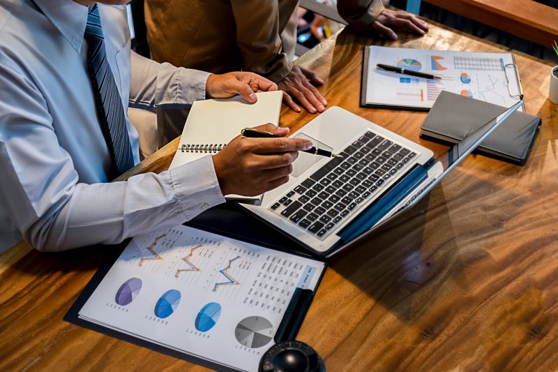 People working on a laptop with charts on the desk.